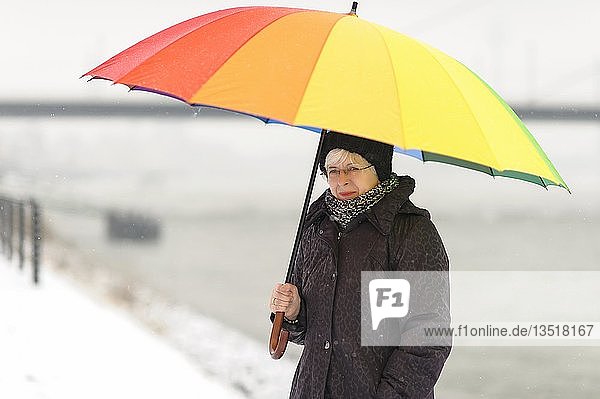 Frau steht mit einem bunten Regenschirm im Winter am Rheinufer  Düsseldorf  Rheinland  Nordrhein-Westfalen  Deutschland  Europa