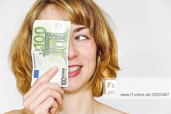 Junge Frau schaut begeistert auf einen 100-Euro-Schein