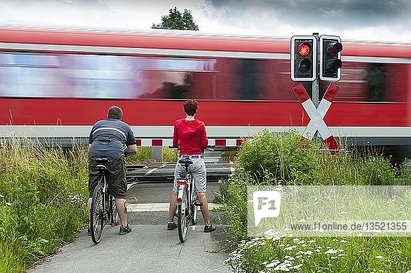 Ein Mann und eine Frau mit Fahrrädern stehen an einem geschlossenen Bahnübergang  Grevenbroich  Nordrhein-Westfalen  Deutschland  Europa