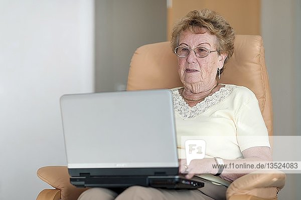 Ältere Frau sitzt auf einem Stuhl mit ihrem Laptop