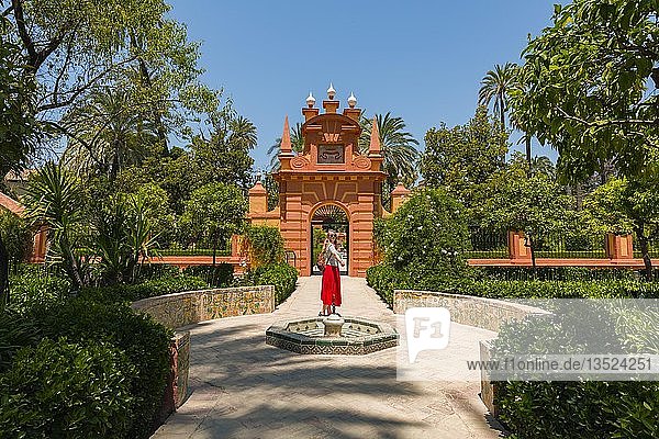 Young woman in red dress in the gardens of the Alcazar  fountain  Royal Palace of Seville  Sevilla  Spain  Europe