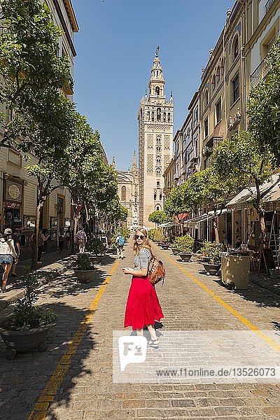 Woman with red dress on street  behind La Giralda  belfry of Seville Cathedral  Catedral de Santa Maria de la Sede  Seville  Andalusia  Spain  Europe