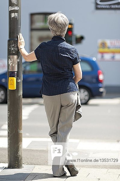 Frau  50+  wartet auf das grüne Licht einer Ampel an einer Kreuzung