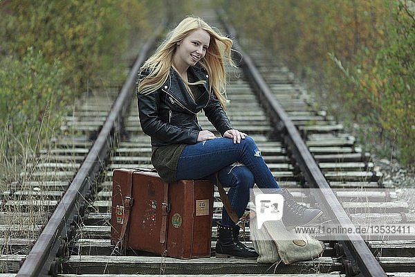 Junge Frau auf einem Koffer sitzend  auf einem Bahngleis  Deutschland  Europa