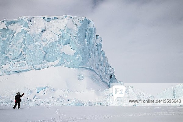 Eisberg  Person in arktischer Kleidung steht auf gefrorenem Fjord  Baffininsel  Davis Straight Küste  Nunavut  Kanada  Nordamerika