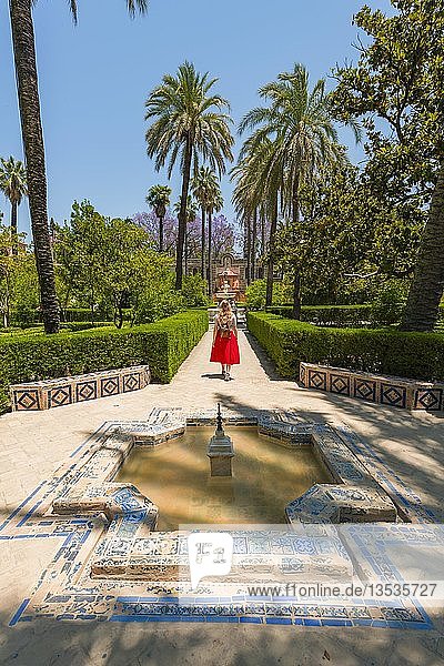 Young woman in red dress is running through gardens of the Alcazar  fountain  Royal Palace of Seville  Sevilla  Spain  Europe