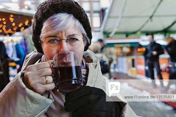 Frau  50+  trinkt Glühwein auf dem Weihnachtsmarkt