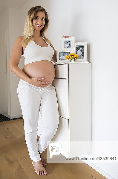 Frau im neunten Monat schwanger  posiert vor Babyfotos mehrerer Generationen  Deutschland  Europa