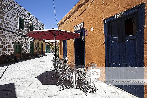 Table and chairs with parasols in front of a cafe  colorful houses  La Atalaya  Gran Canaria  Canary Islands  Spain  Europe