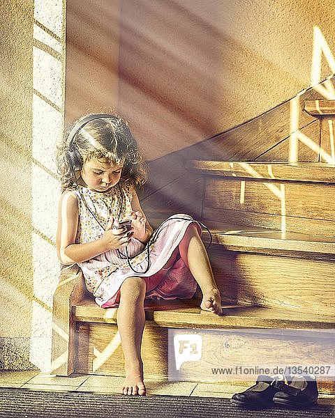 Mädchen  3 Jahre alt  sitzt auf einer Treppe und hört mit Kopfhörern Musik  Deutschland  Europa