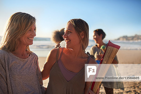 Happy mother and daughter with yoga mat on sunny beach during yoga retreat