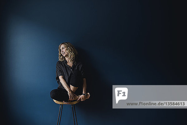 Portrait carefree woman sitting on stool against blue background