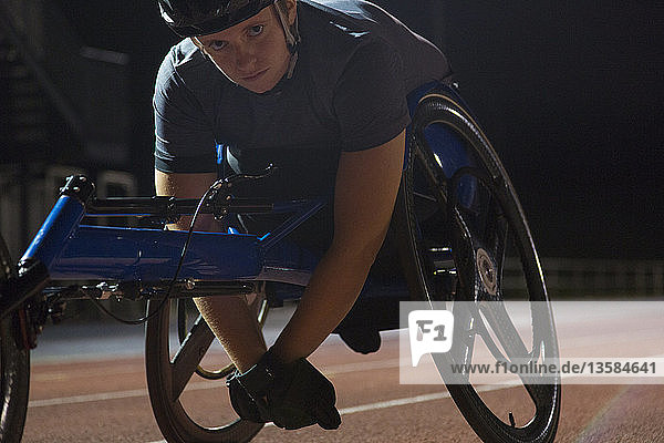 Portrait determined young female paraplegic athlete training for wheelchair race on sports track at night