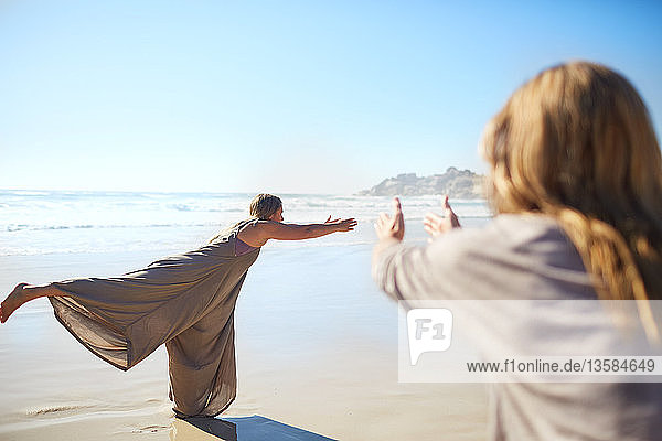Woman practicing warrior 3 pose on sunny beach during yoga retreat