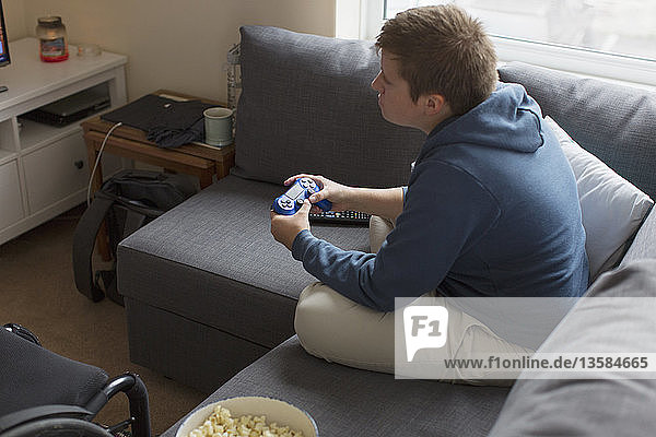 Young woman playing video game on sofa next to wheelchair