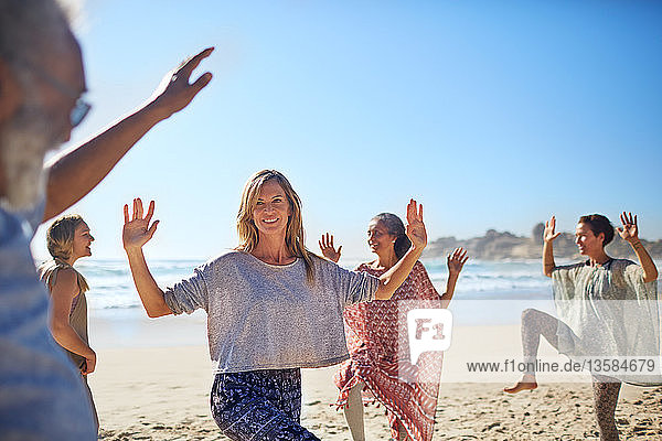 Group dancing on sunny beach during yoga retreat