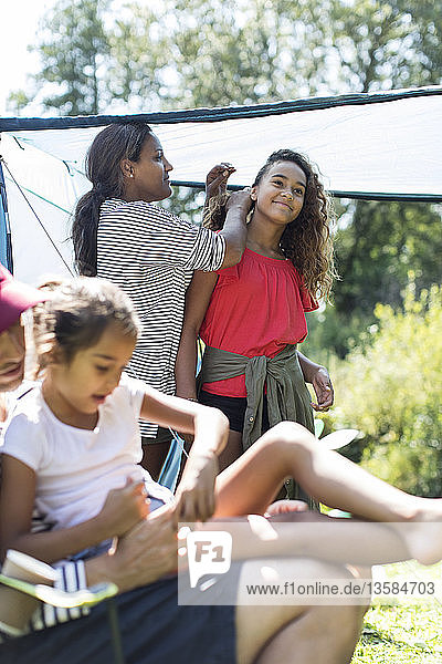 Mother fixing daughters hair at campsite