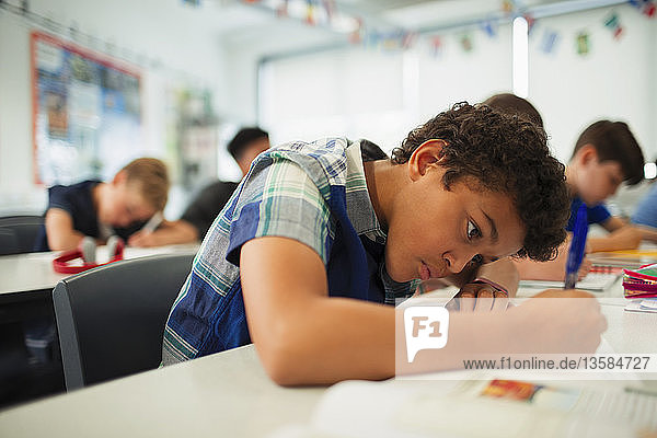Konzentrierter Junge der Junior High School bei den Hausaufgaben im Klassenzimmer
