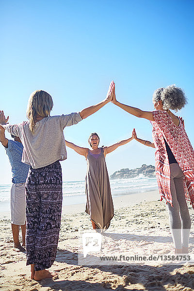 Gruppe  die sich am sonnigen Strand während eines Yoga-Retreats im Kreis an den Händen fasst