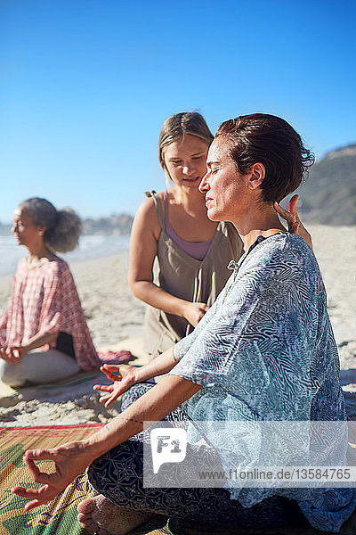 Gelassene Frau meditiert am sonnigen Strand während eines Yoga-Retreats