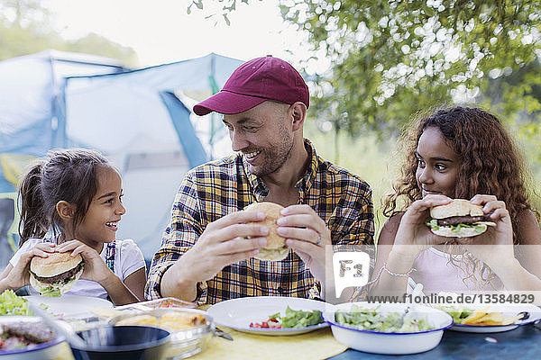 Vater und Töchter genießen einen Hamburger vom Grill auf dem Campingplatz