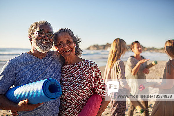 Portrait glückliches älteres Paar mit Yogamatten am sonnigen Strand während eines Yoga-Retreats