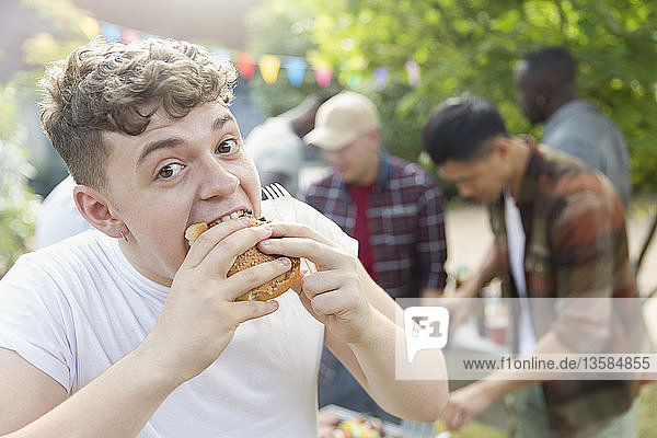 Portrait hungry teenage boy eating hamburger at backyard barbecue