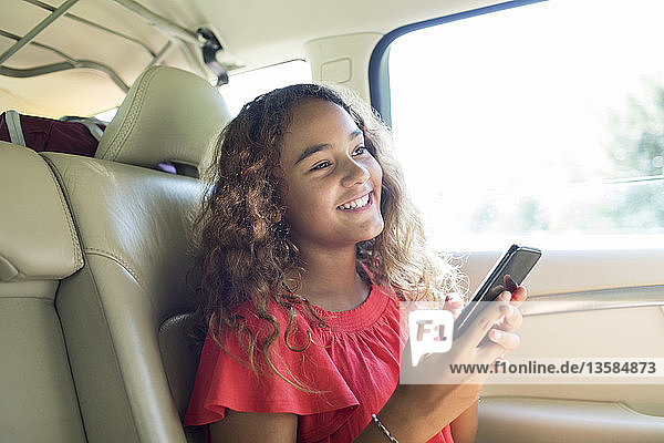 Lächelndes Mädchen mit Smartphone auf dem Rücksitz eines Autos