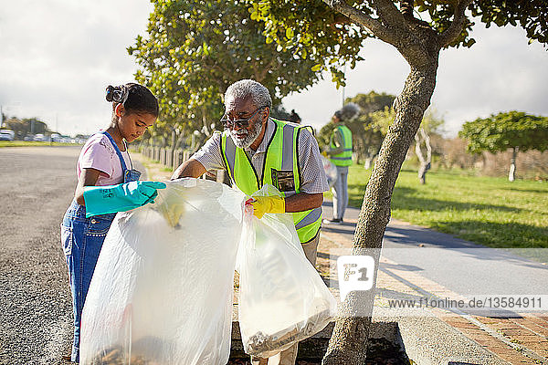 Grandfather and granddaughter volunteers cleaning up litter in sunny park