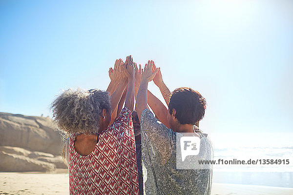 Frauen mit erhobenen Armen im Kreis am sonnigen Strand während eines Yoga-Retreats