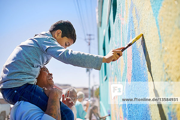 Vater und Sohn malen als Freiwillige ein Wandgemälde an eine sonnige Wand