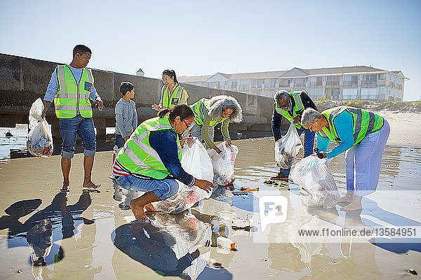 Freiwillige beseitigen Müll am sonnigen  nassen Sandstrand