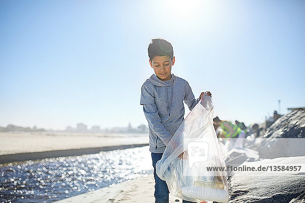 Freiwilliger Junge räumt Müll am sonnigen Strand auf