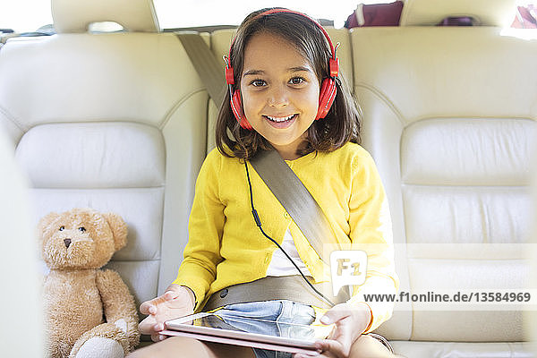 Portrait smiling confident girl watching movie with headphones and digital tablet in back seat of car