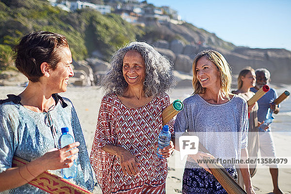 Women friends with yoga mats talking on sunny beach during yoga retreat