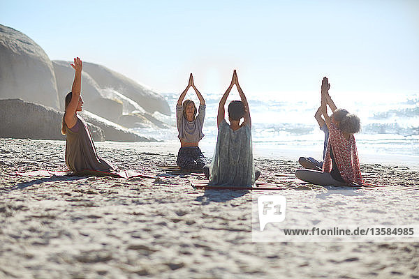 Serene people in circle meditating on sunny beach during yoga retreat