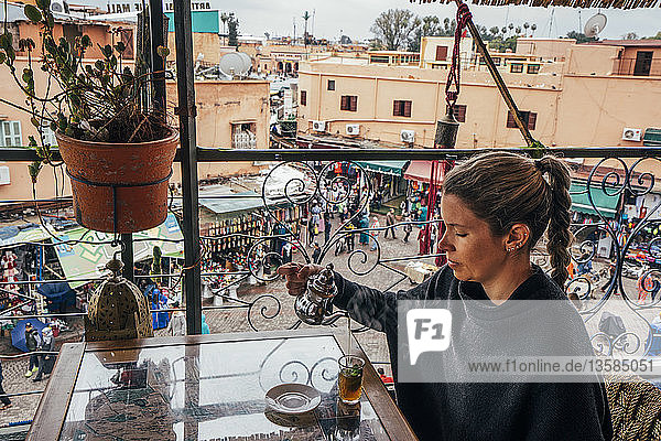 Frau genießt Tee auf einem Balkon mit Blick auf den Straßenmarkt  Marrakesch  Marokko