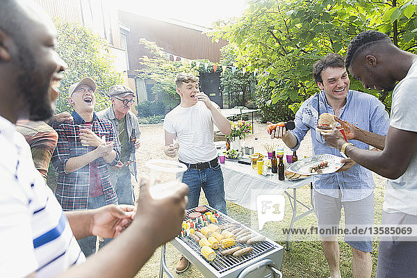 Männliche Freunde lachen und essen um einen Grill im Hinterhof