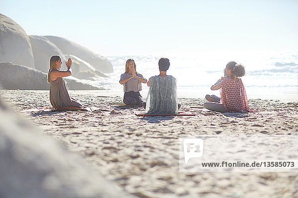Group meditating in circle on sunny beach during yoga retreat