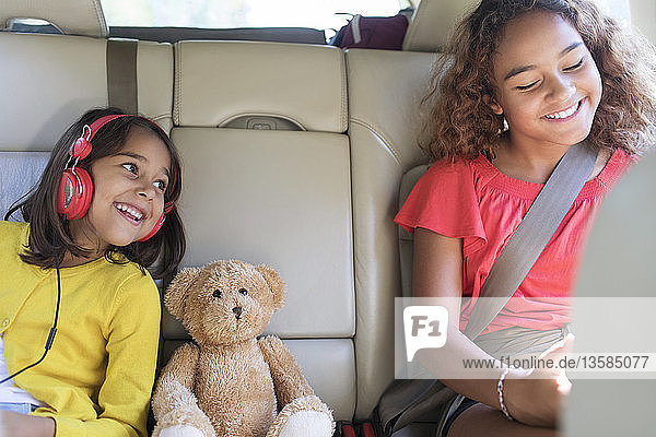 Happy sisters and teddy bear riding in back seat of car