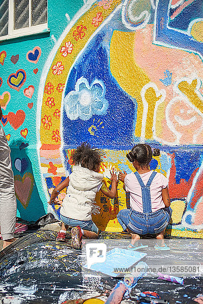 Mädchen malen ein lebendiges Wandgemälde an eine sonnige Wand