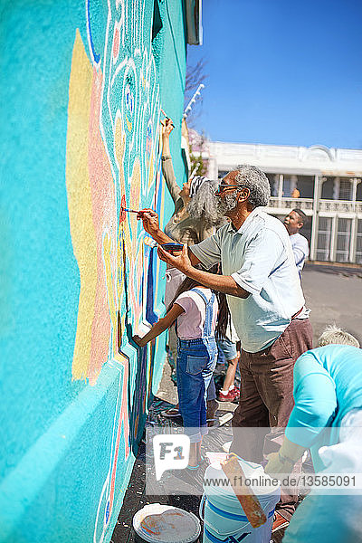 Freiwillige aus der Gemeinschaft malen ein lebendiges Wandgemälde auf eine sonnige Stadtmauer