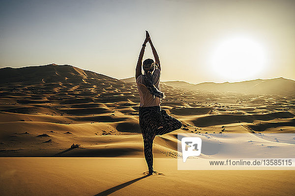 Gelassene Frau in Yoga-Baum-Pose in sonniger Sandwüste  Sahara  Marokko