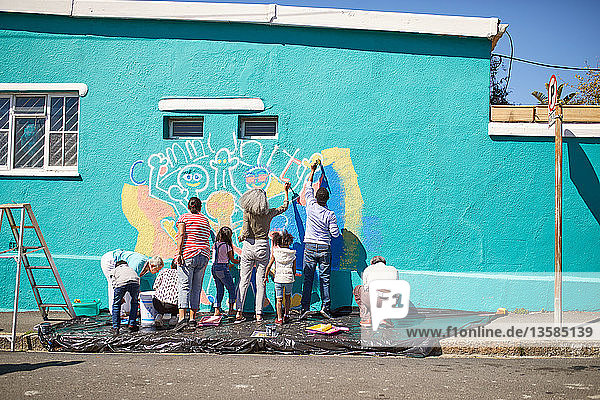 Freiwillige aus der Gemeinschaft malen ein lebendiges Wandgemälde auf eine sonnige Stadtmauer