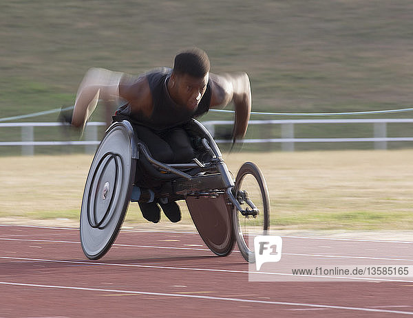 Determined young male paraplegic athlete speeding along sports track during wheelchair race