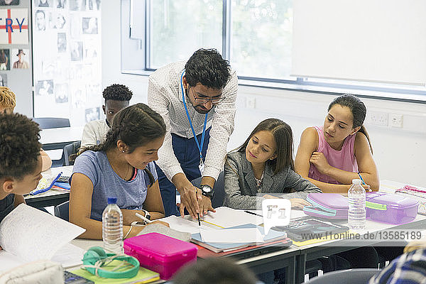 Ein männlicher Lehrer hilft einer Schülerin am Schreibtisch im Klassenzimmer