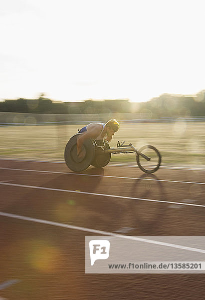 Entschlossener junger querschnittsgelähmter Sportler  der in einem Rollstuhlrennen über eine Sportstrecke rast