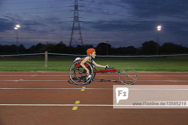 Jugendliche querschnittsgelähmte Sportlerin im Rollstuhl fährt nachts auf einer Sportbahn