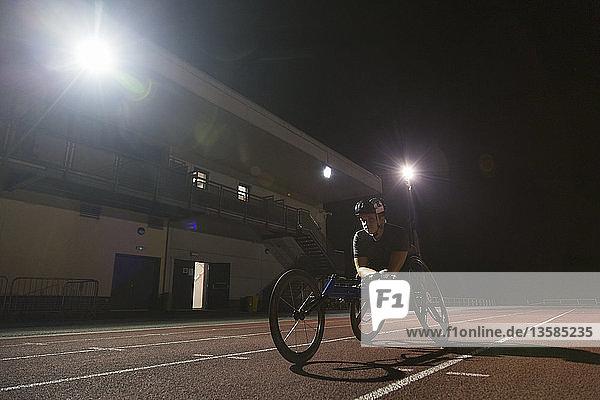 Determined female paraplegic athlete training for wheelchair race on sports track at night
