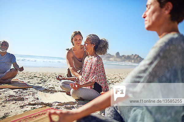 Gelassene Frauen meditieren am sonnigen Strand während eines Yoga-Retreats